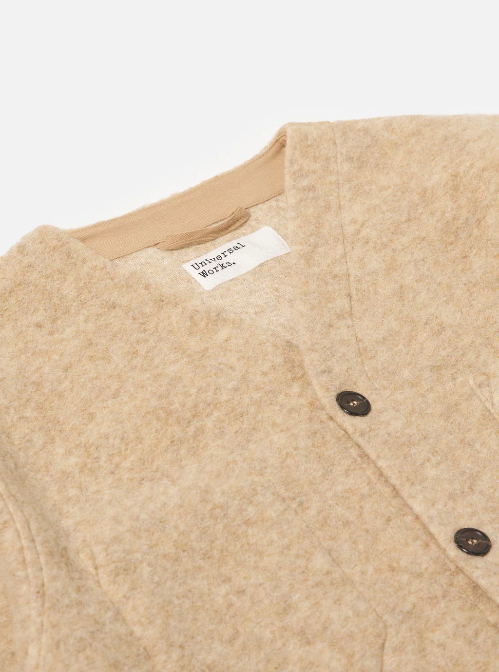 Close-up of Universal Works beige textured cardigan with a label on a white background