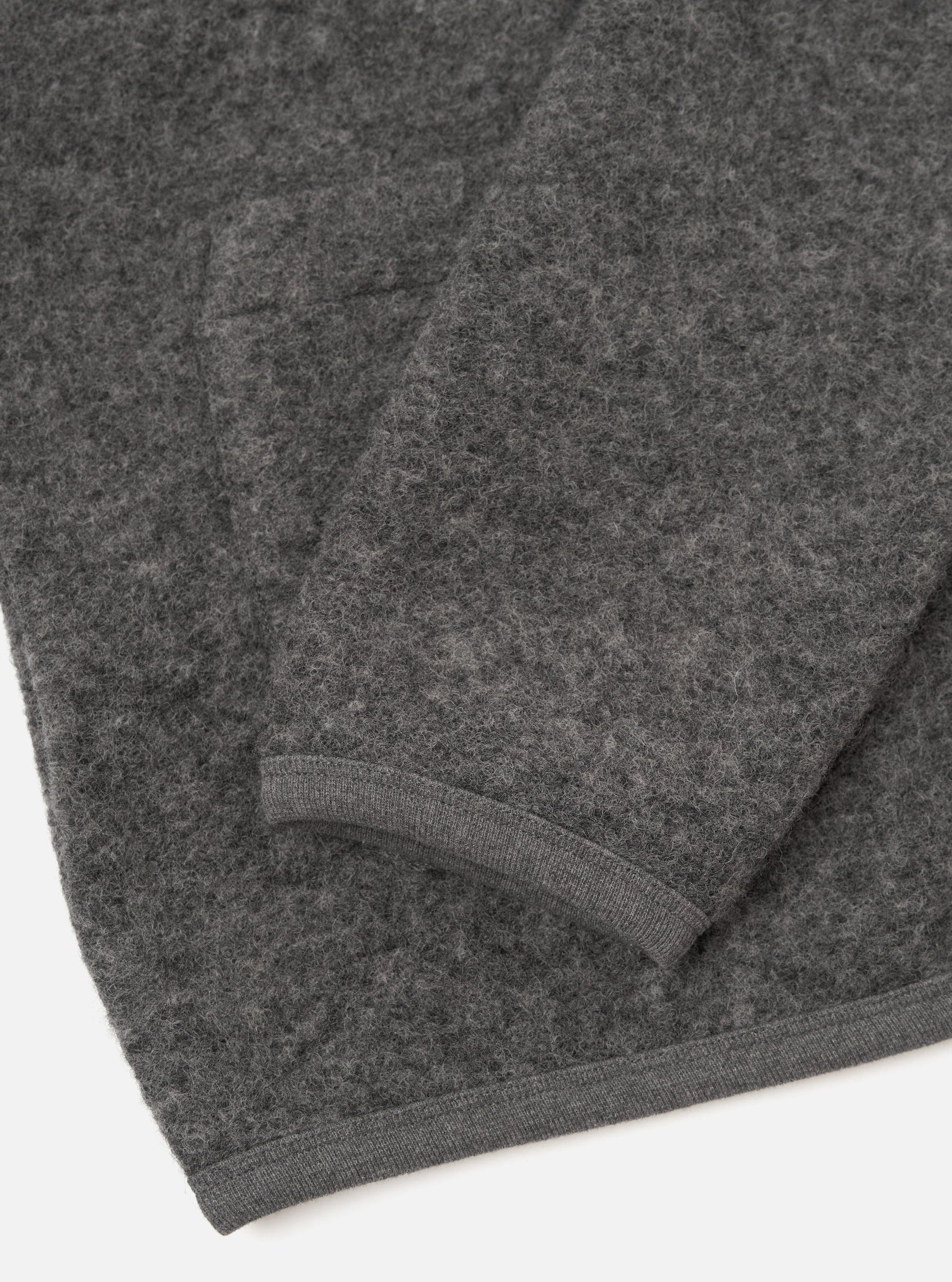 Close-up of a dark grey marl Universal Works Fleece cardigan showing the texture and ribbed cuff detail against a plain white background.