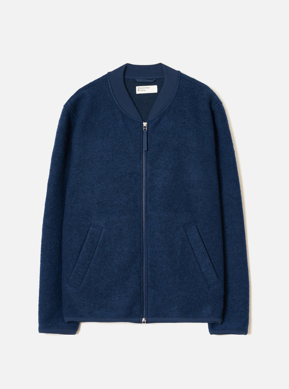 Universal Works Indigo wool fleece Bomber jacket with a zip against a light grey background 