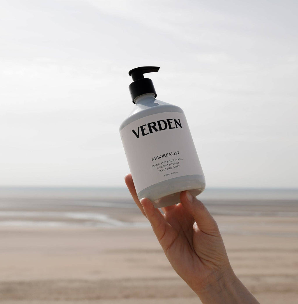 Hand holding a bottle of Verden soap with a beach in the background