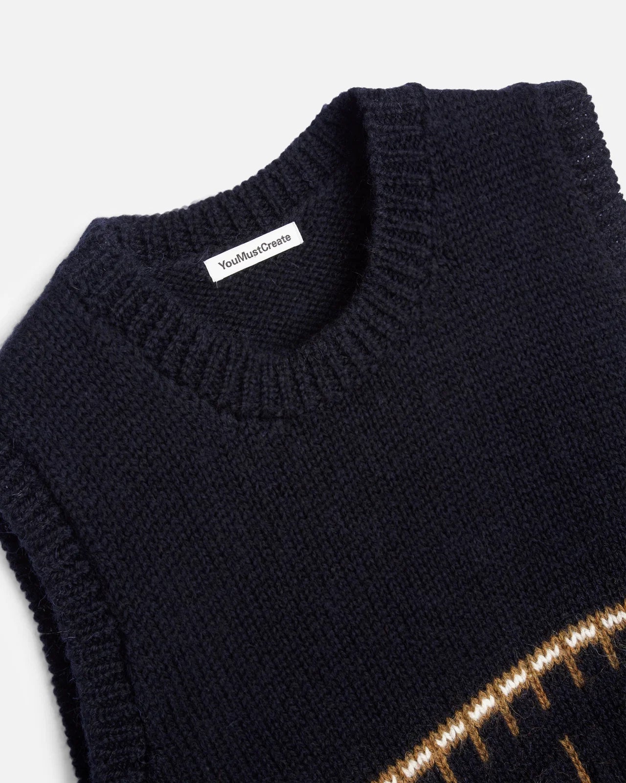Close-up of a black ribbed knit sweater with a white neck label reading 'YouMustDream' and a gold patterned accent at the bottom.