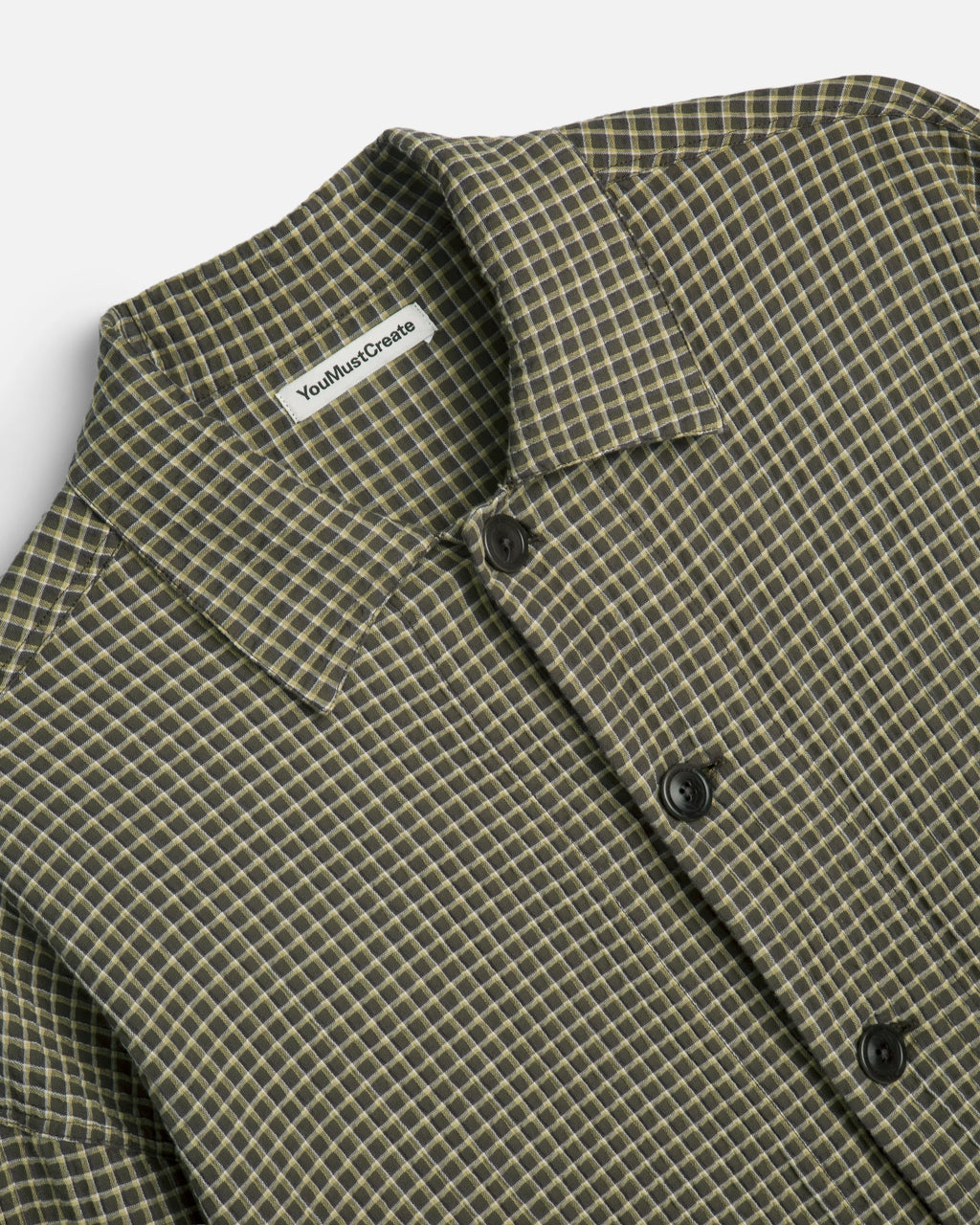 Close-up of a collared button-front shirt with a small-scale check pattern in olive green and beige. 