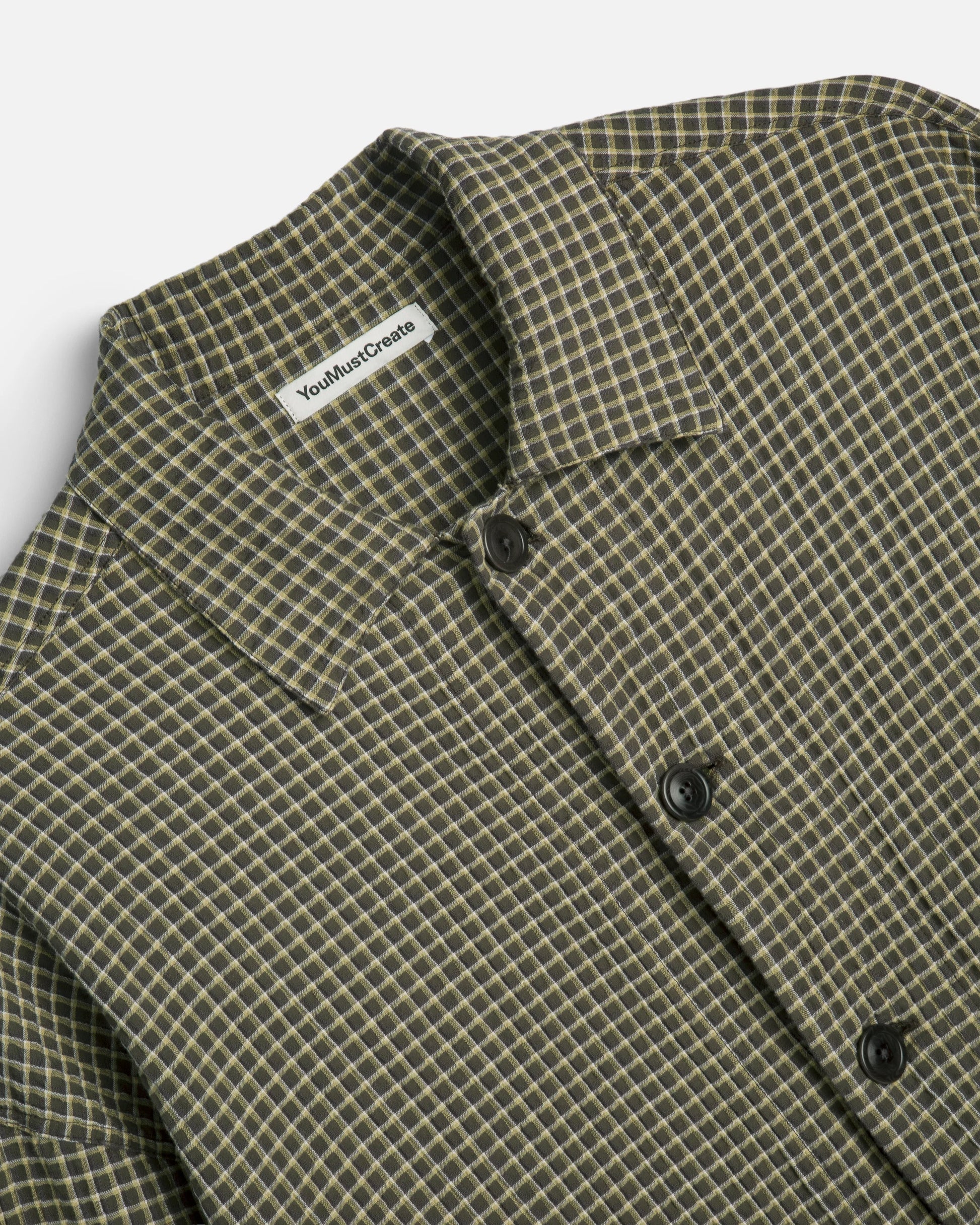 Close-up of a collared button-front shirt with a small-scale check pattern in olive green and beige. 