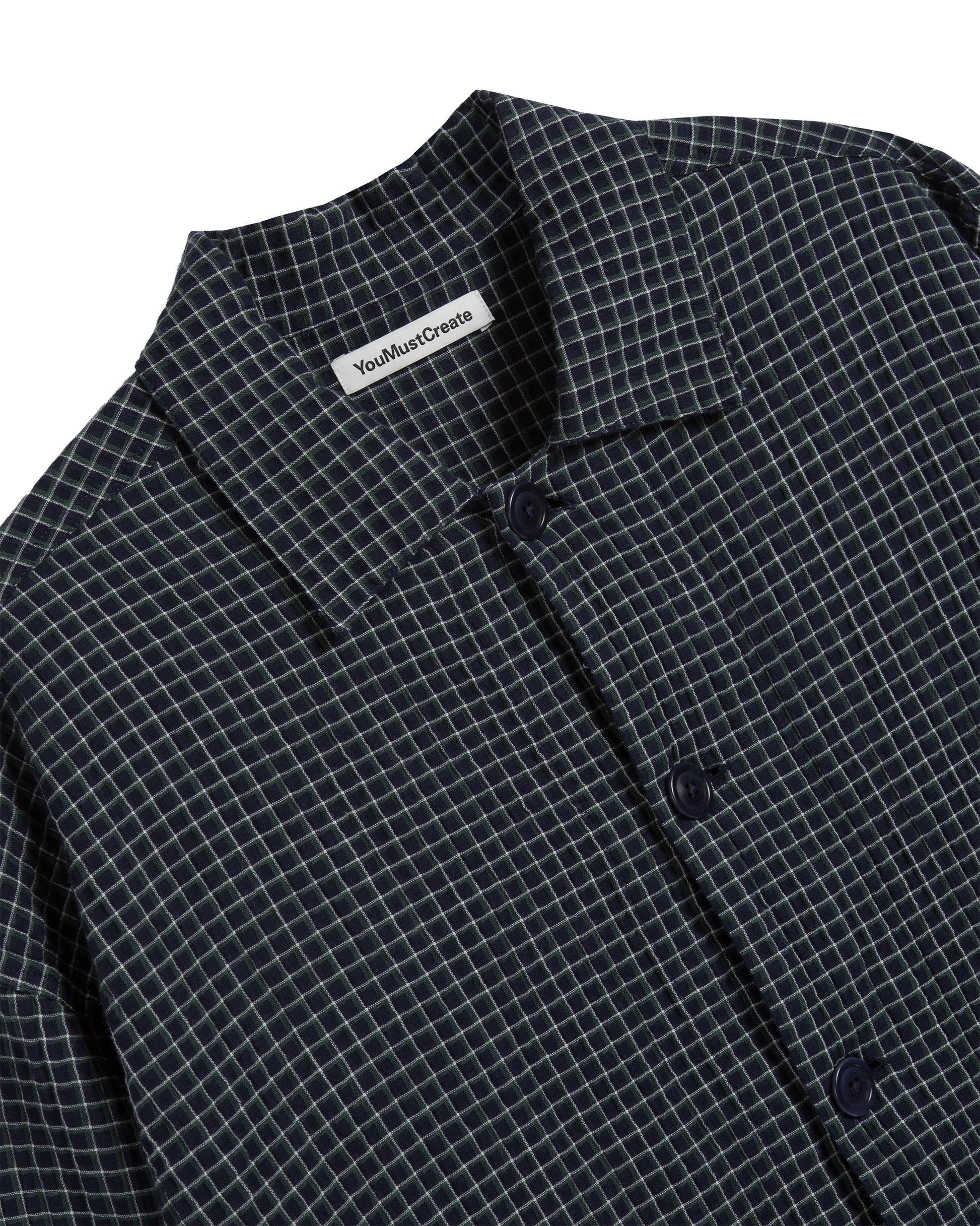 Close-up of a navy, green and white checkered shirt with a YMC label on a white background