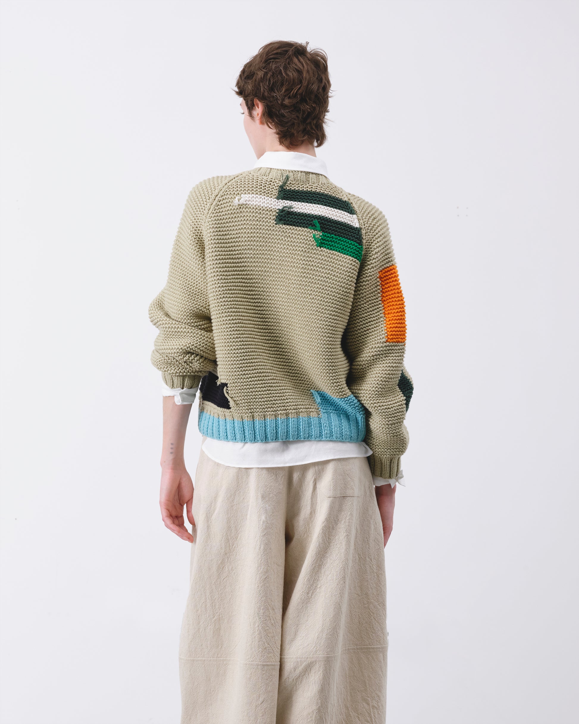 Person wearing a patterned sweater with color-blocked sleeves on a white background