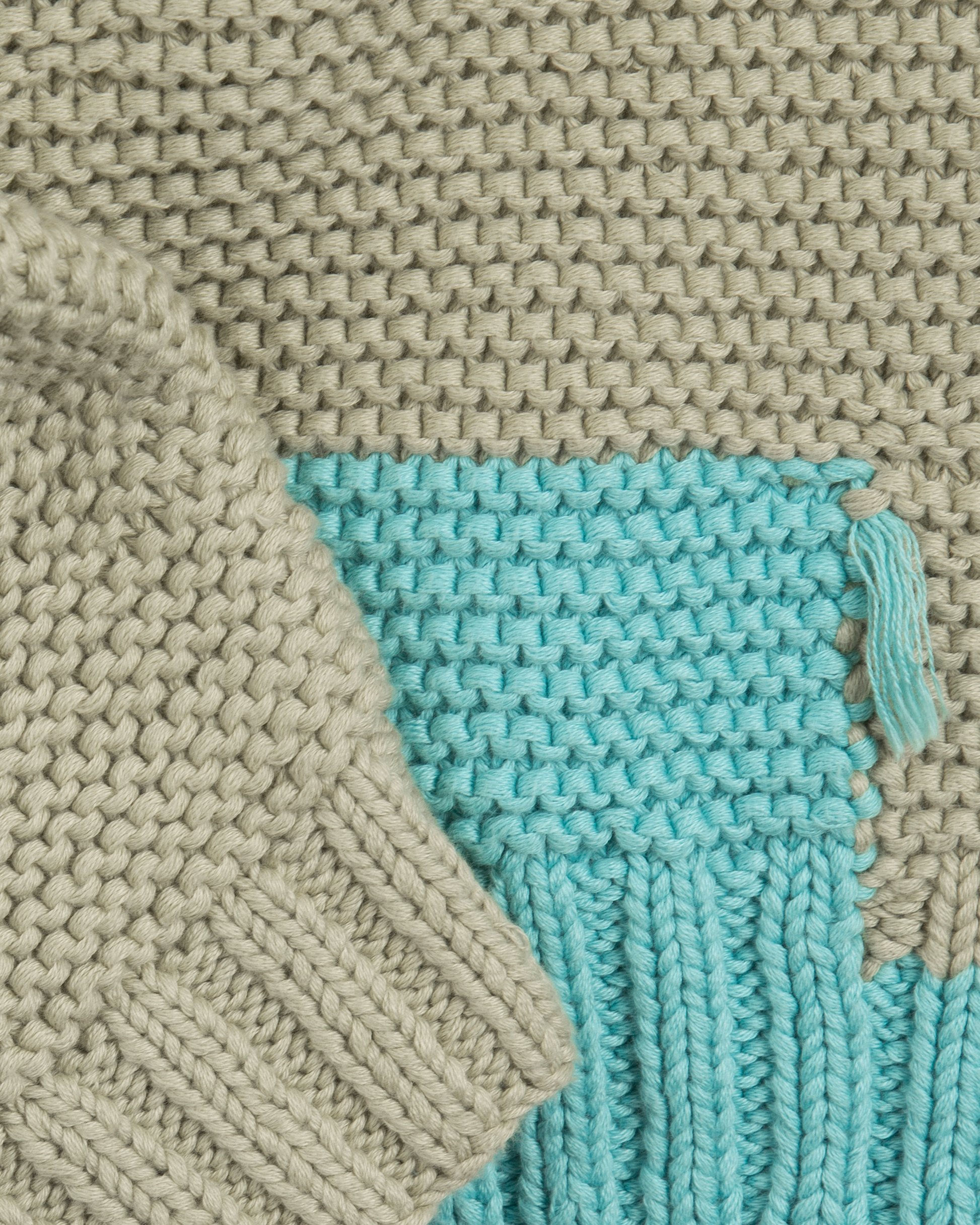 Close-up of a knitted cardigan with a blue corner and beige fabric.
