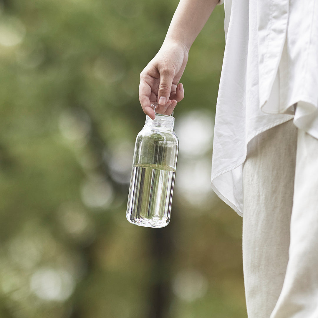 Person holding a clear glass bottle with a blurred green background