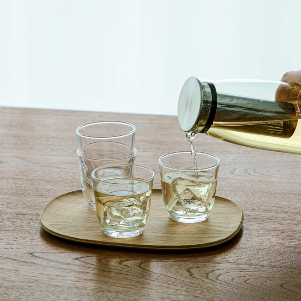 Glass carafe pouring liquid into four glasses on a wooden tray.