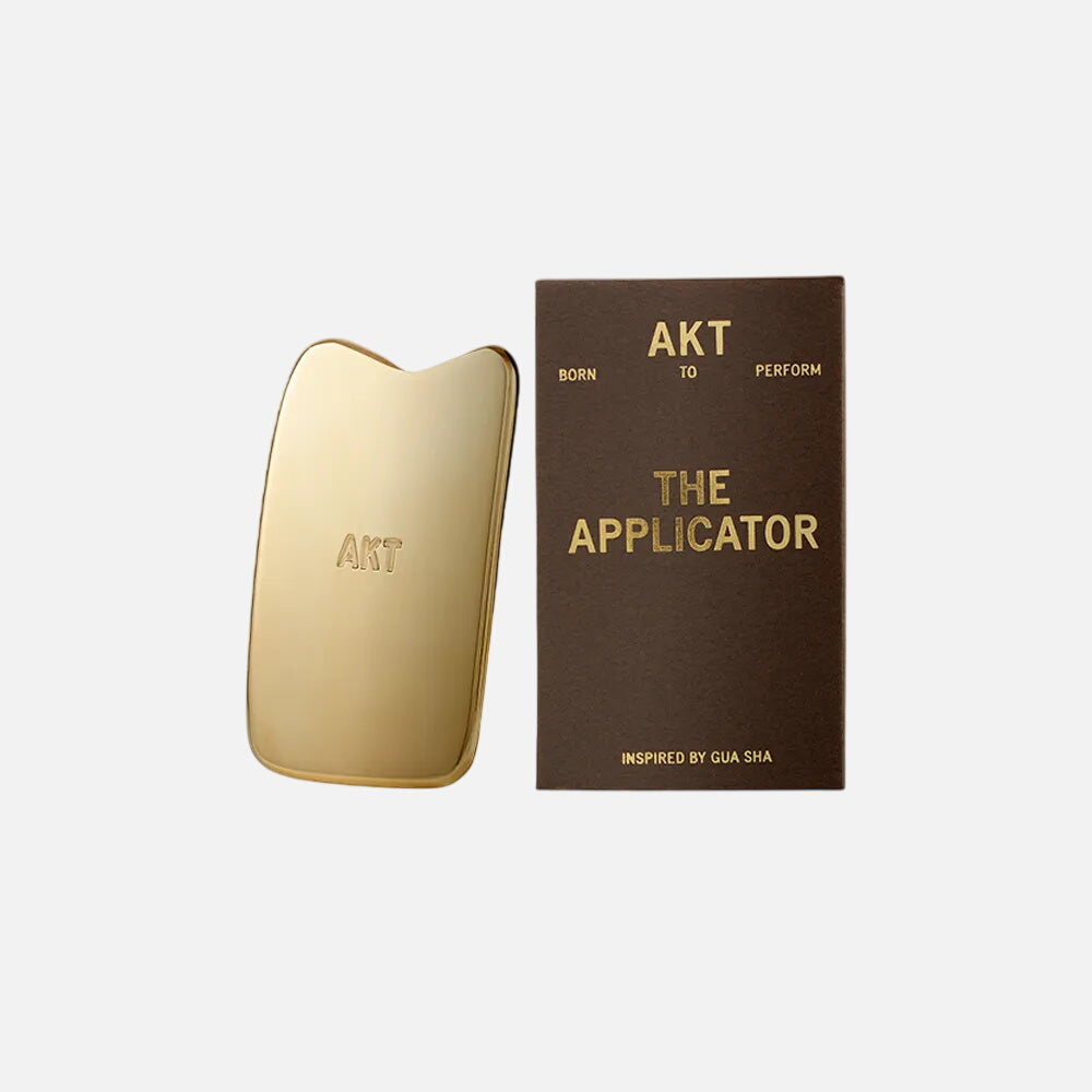 Gold applicator and brown box with 'AKT' branding on a beige background