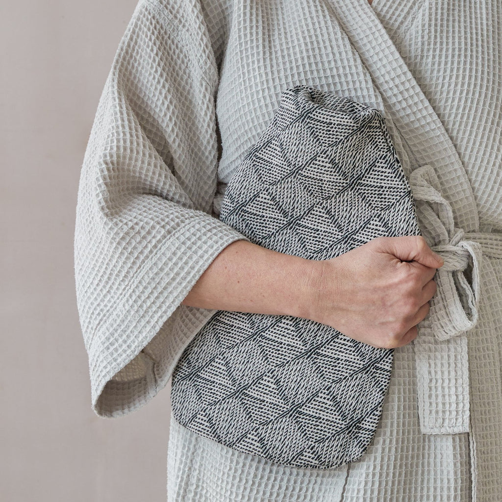 Person holding a textured gray pot holder with a beige robe